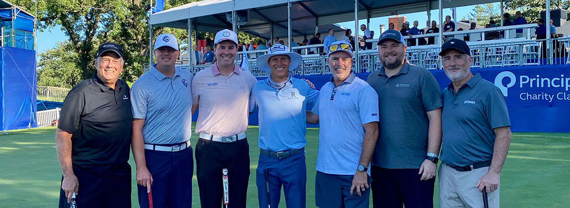 Seven men smiling for a photo on a golf course